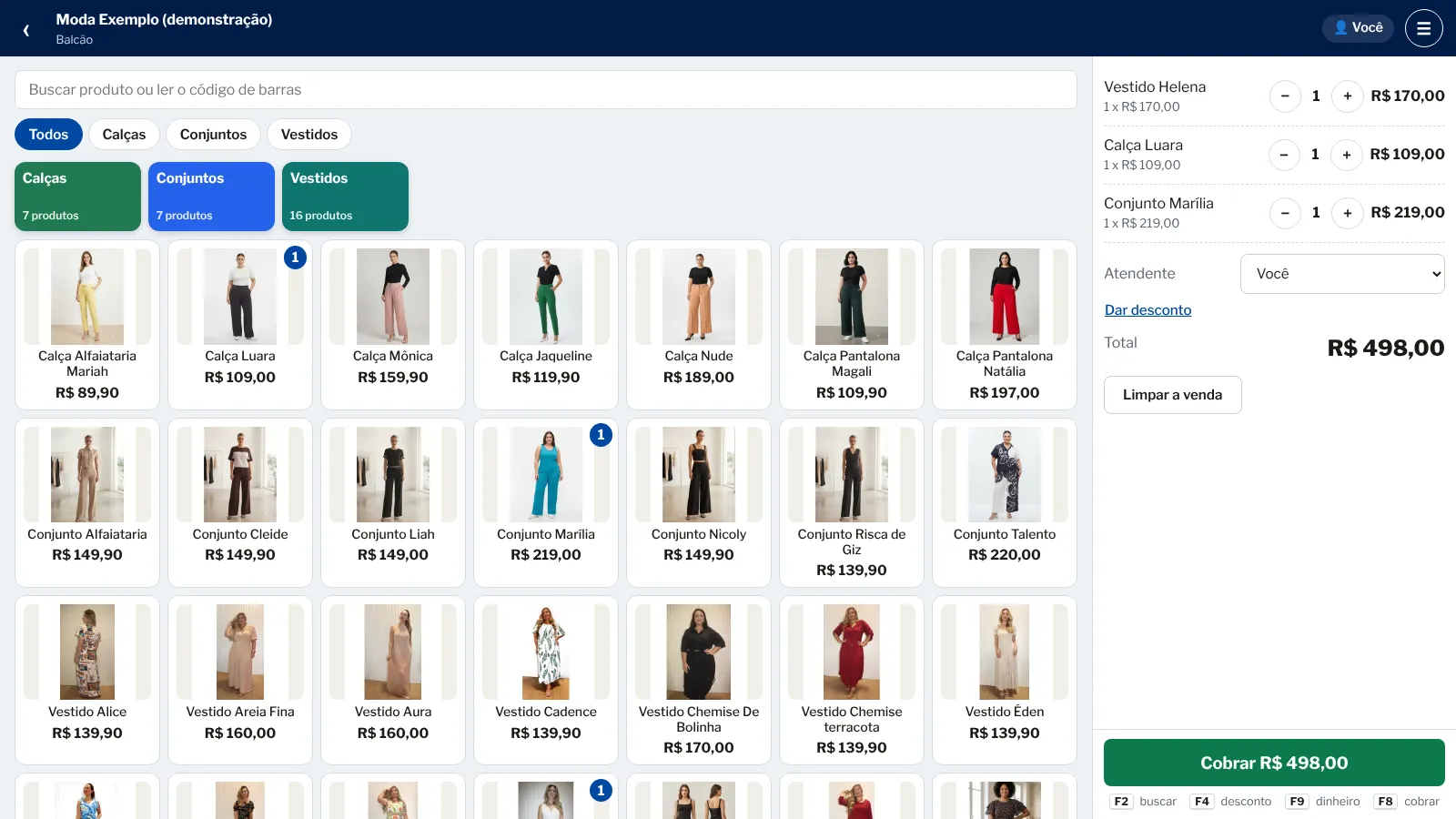 O caixa no computador com vestidos, calças e conjuntos, cada peça com a sua foto.